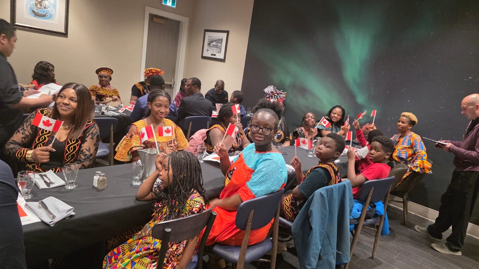 Families in traditional dress waving Canadian flags at RLRI's Multiculturalism Day